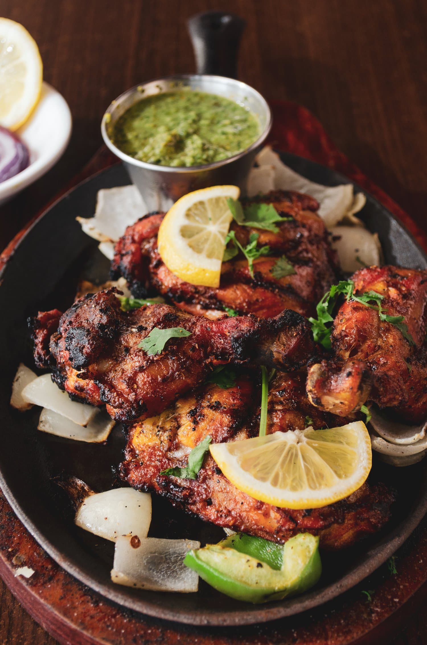 Grilled chicken drumsticks on a charcoal skillet with lemon, cilantro and onions