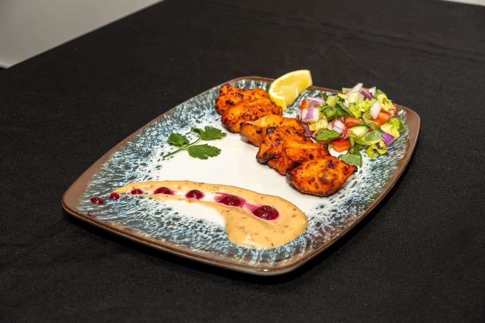 Grilled chicken tikka skewers with fresh salad and a lemon wedge
