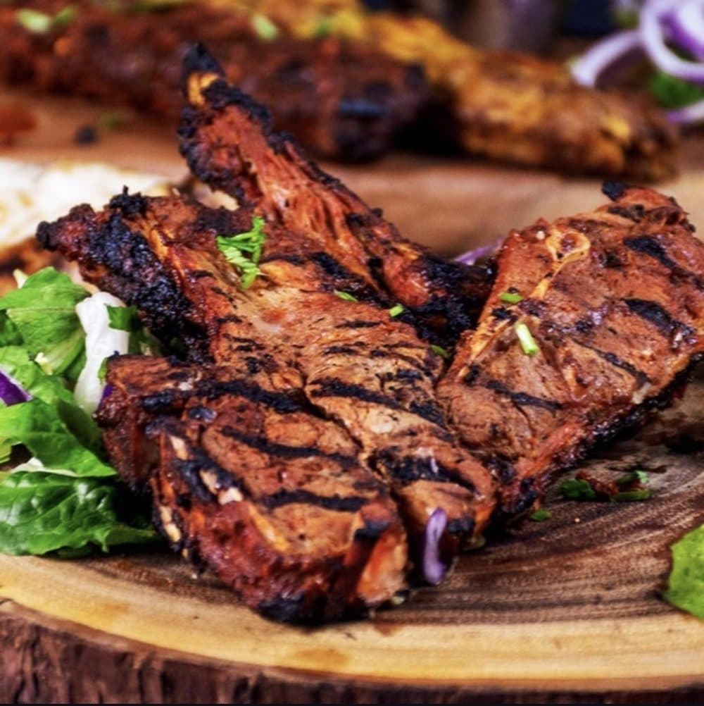 Grilled bone-in lamb chops with char marks, served with salad and pickled red onion
