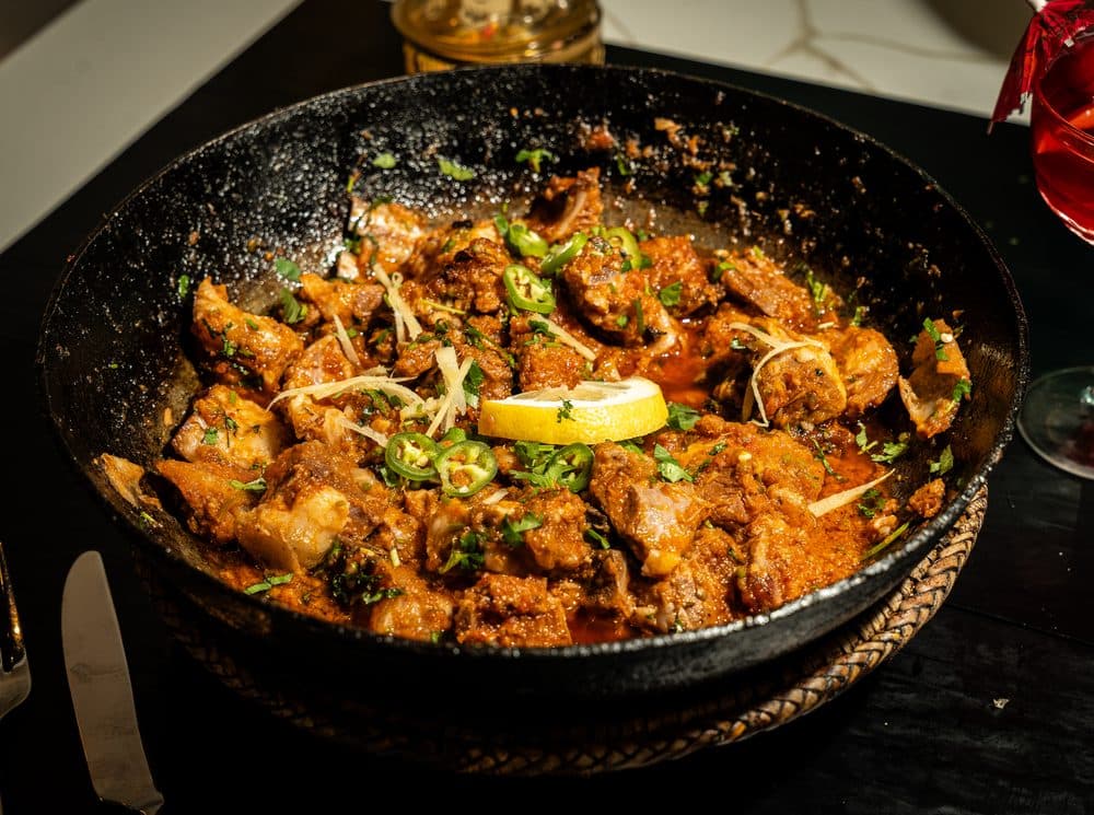 Lamb karahi in a cast iron karahi, garnished with lemon, ginger and green chilies