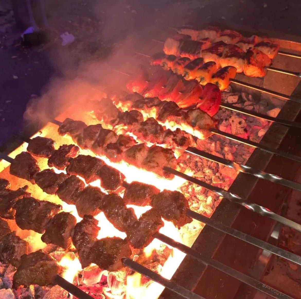 Skewers of meat grilling over an open flame for a catered event